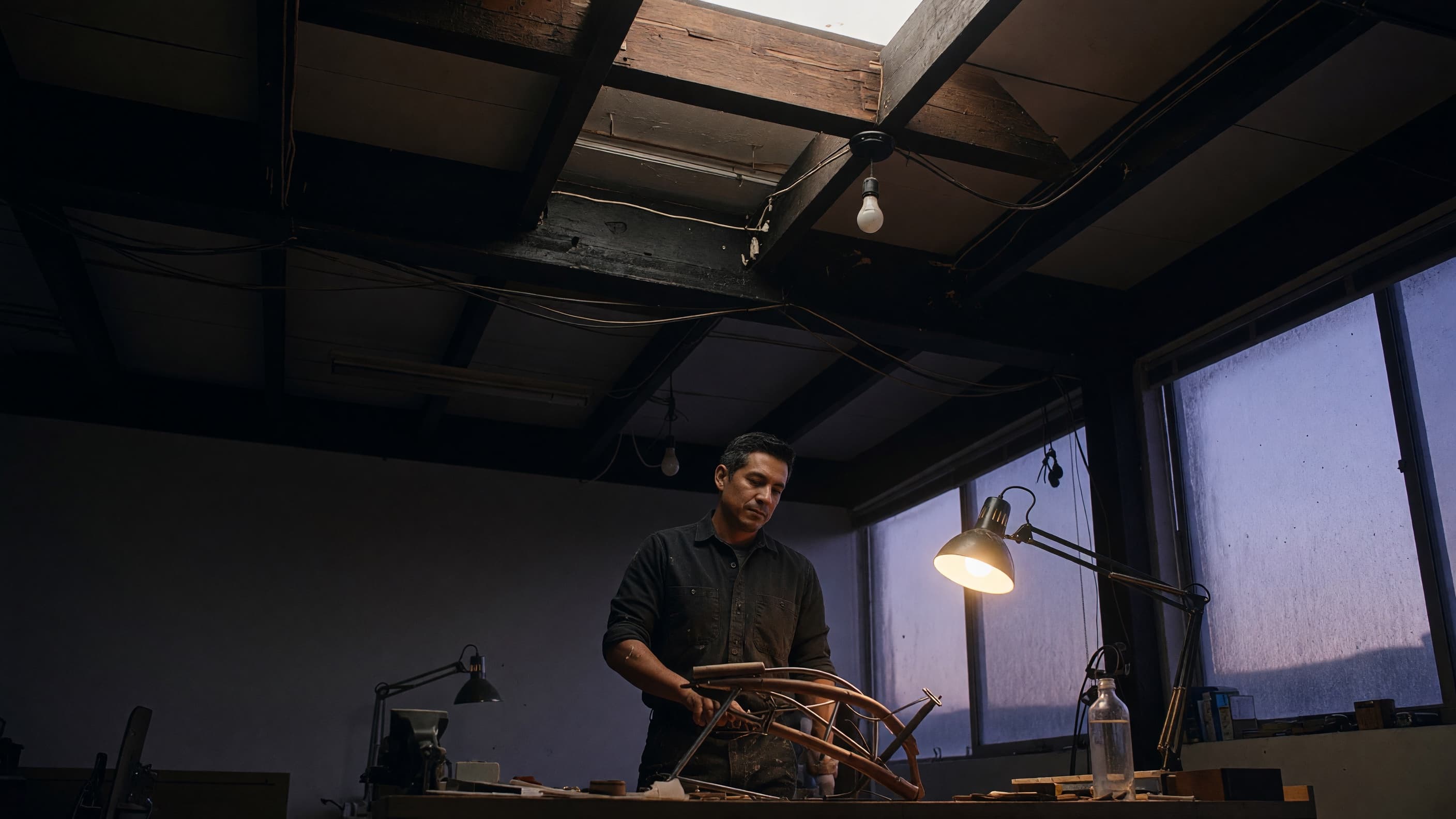 A craftsman at a dusk-lit workbench, studying a physical project with calm focus.